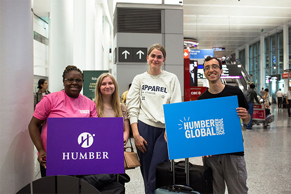 4 students at airport - 2 holding Humber sign