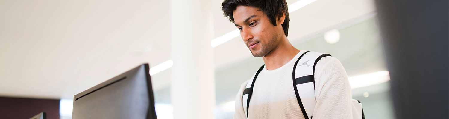 male student standing in front of a computer