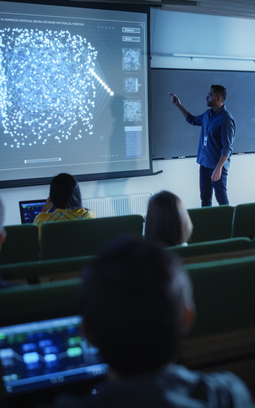 University lecturer explaining a neural network visualization on a large screen to students in a classroom setting