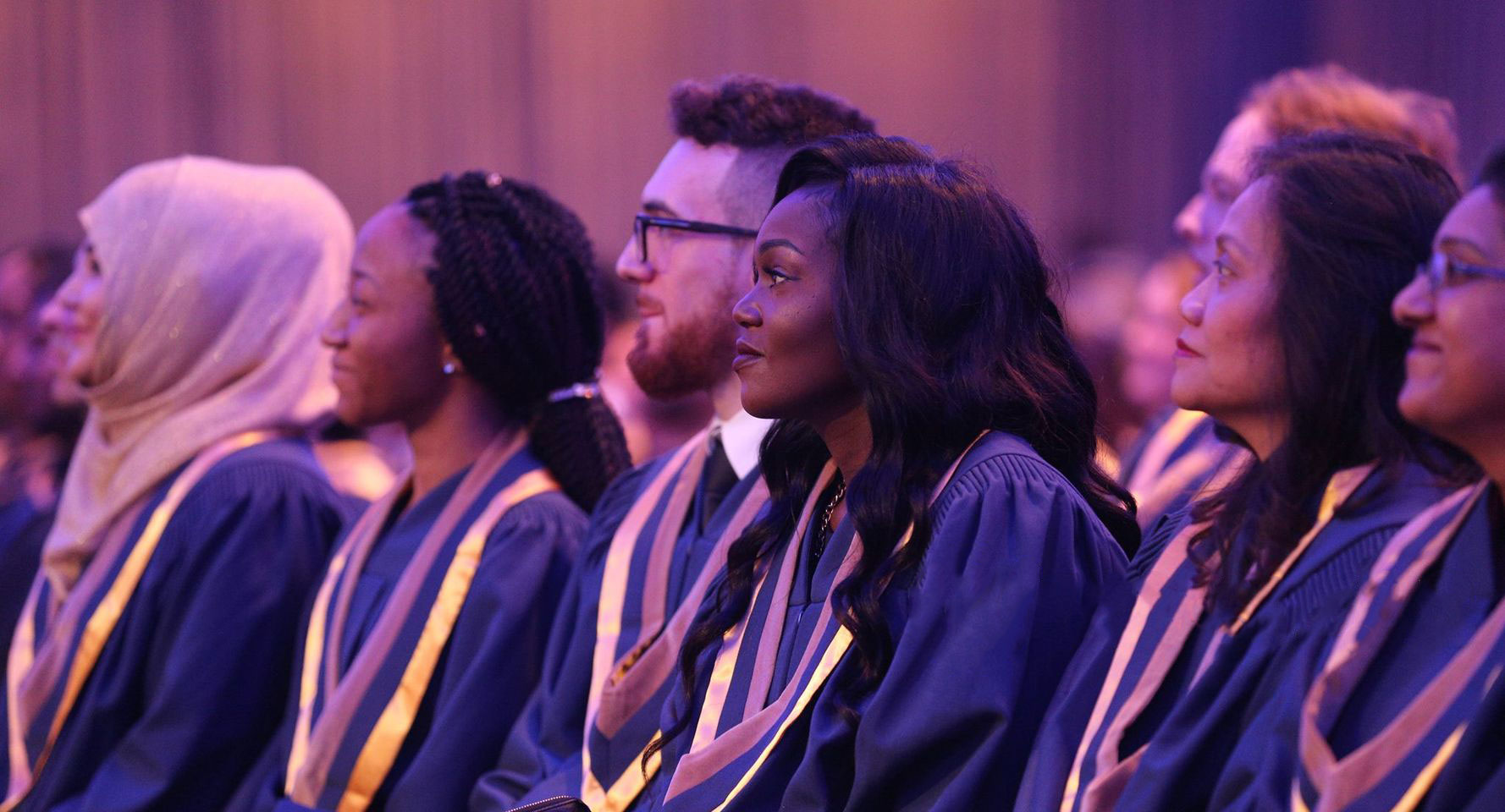 Diverse set of Humber graduates in gowns looking toward a stage