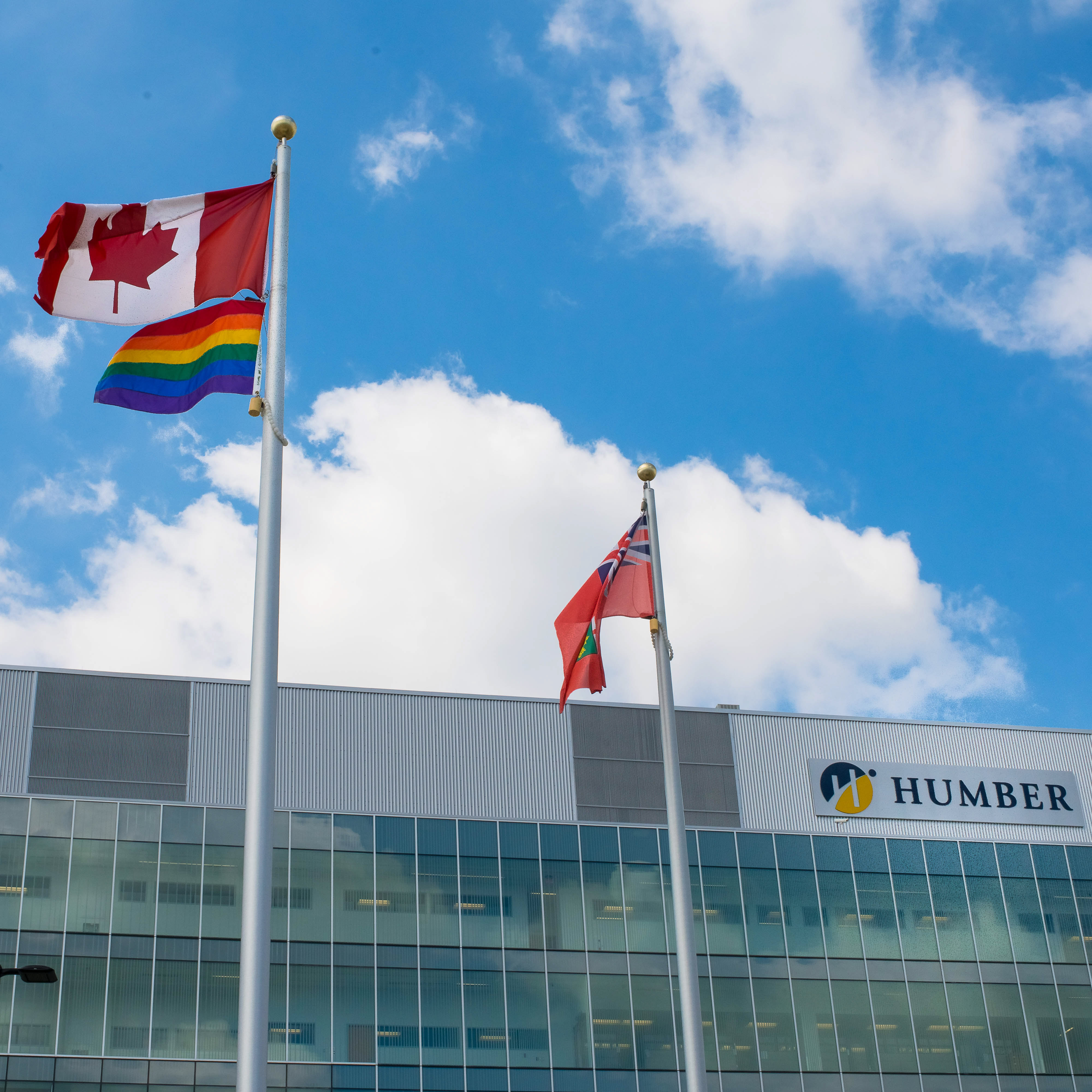 Humber behind a Canada flag, pride flag and the flag of Ontario