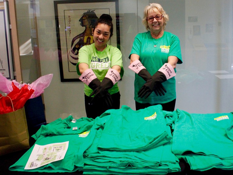 two volunteers with "Queen of clean" gloves standing behind the green t-shirt pile