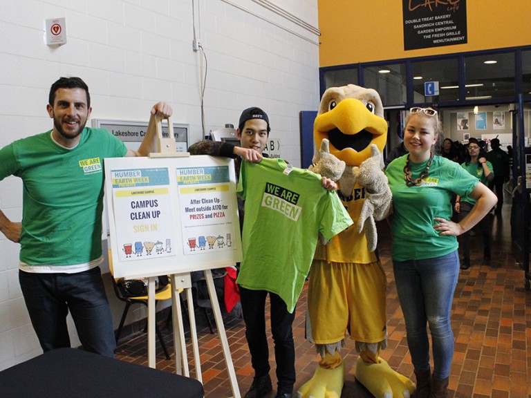 three volunteers posing with the humber hawk mascot next to the sign in table