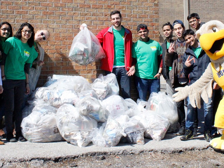 a group of volunteers and the humber hawk mascot posing with a pile of full garbage bags 