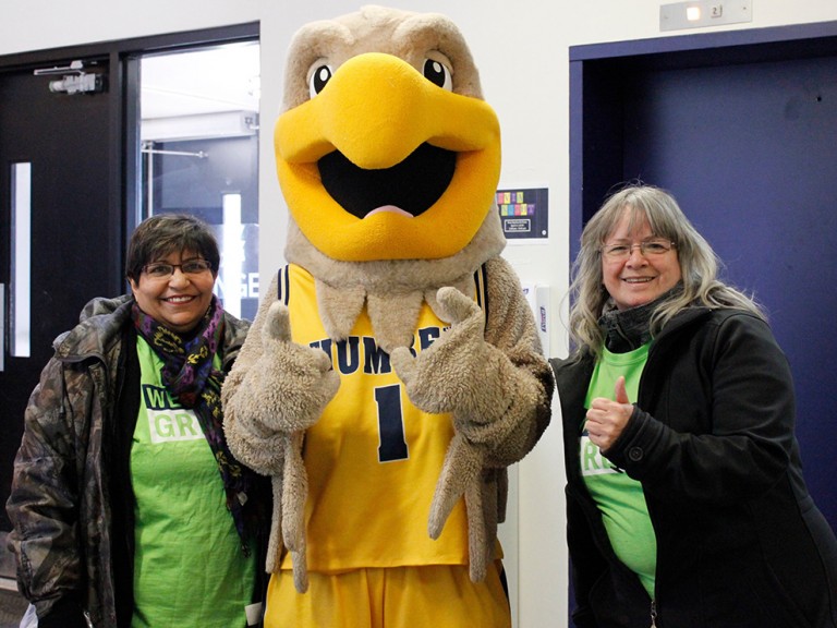 Humber hawk mascot giving the thumbs up with two volunteers posing beside him