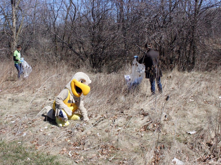 two volunteers and the humber hawk mascot picking up trash outside
