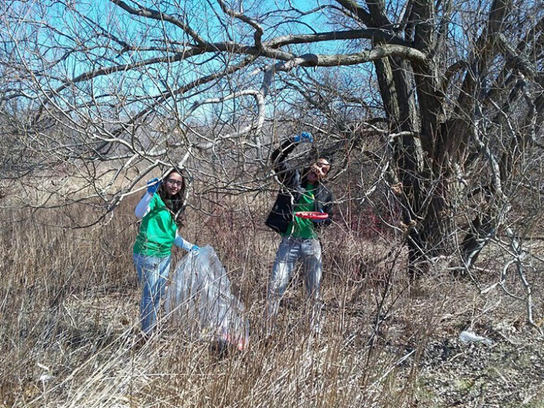 two volunteers picking up litter outside by a tree