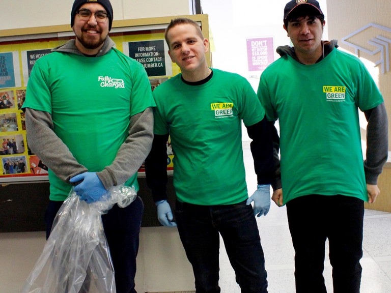 three volunteers posing while one of them holds a garbage bag