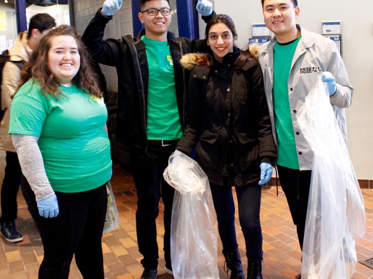 4 volunteers smiling for the photo, two of them hold clear garbage bags