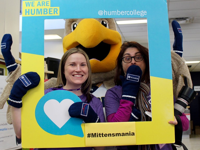 two women posing the humber hawk mascot and their mittens
