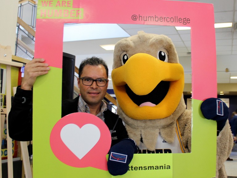 a man and the humber hawk mascot posing behind a photo frame