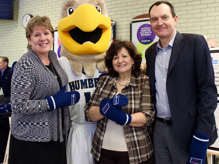 Wanda Buote, Chris Whitaker and another woman posing with the humber hawk mascot while wearing mittens