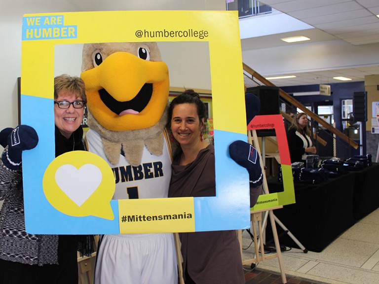 two women holding a photo frame posing with the humber hawk mascot for a photo