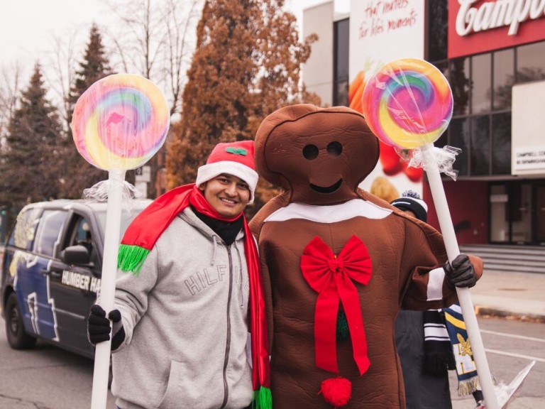 person holding a giant lollypop posing with a person in a gingerbread man costume