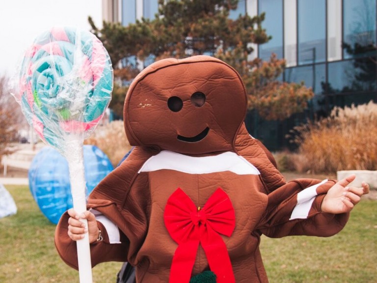person dressed in gingerbread man costume posing with a giant lolly pop