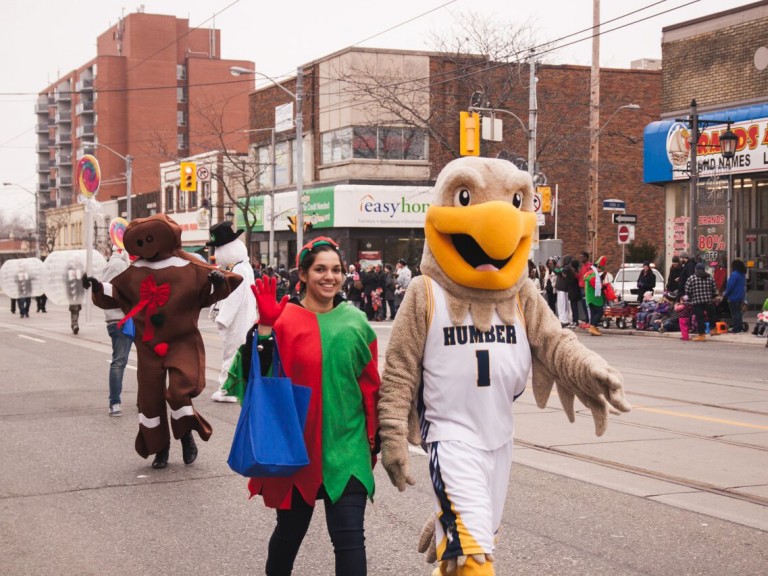 humber hawk mascot walking in the parade beside someone in an elf costume