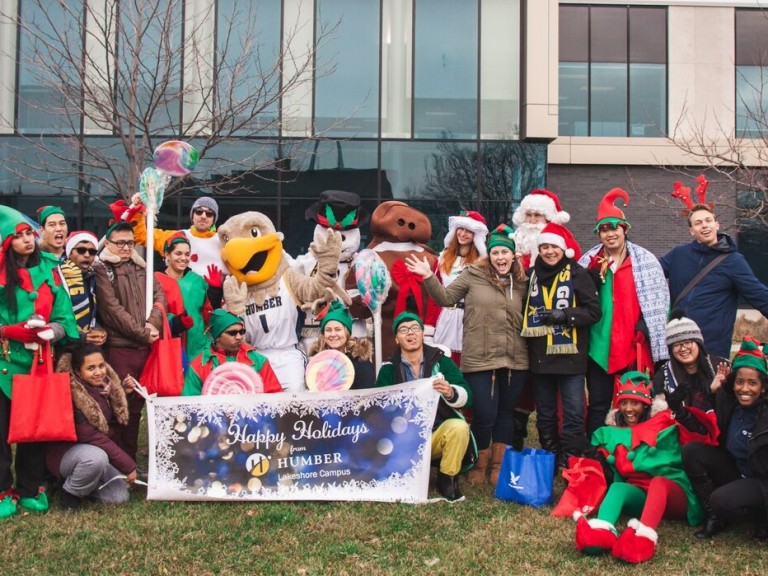 Large group dressed up as elves with the humber hawk mascot posing for a photo