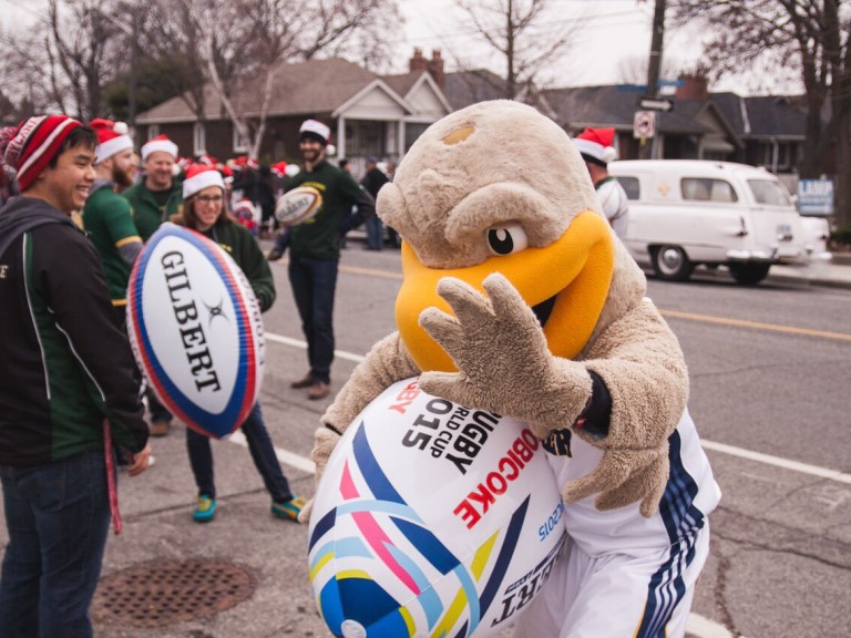 humber hawk mascot holding a large blowup rugby ball with his one hand up