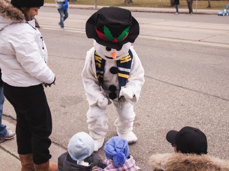 person in snowman costume crouching down to talk to kids in the crowd