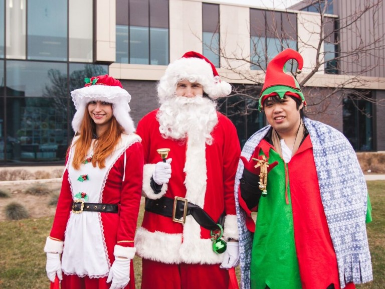 three people posing dressed as Mrs. Clause, Santa Clause and an elf