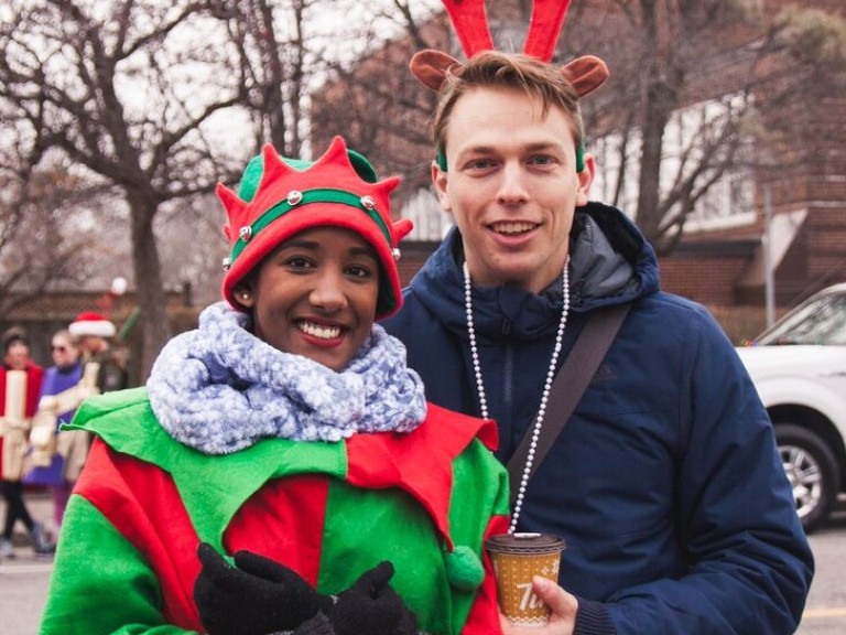 person in an elf costume posing with a person wearing reindeer antlers