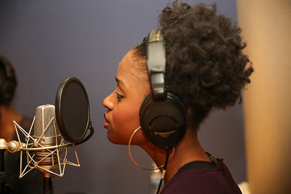 Student wearing headphones singing into a microphone in a sound studio