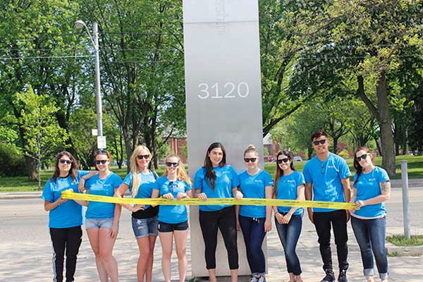 people dressed in blue t-shirts standing in front of a pillar that says 3120 holding a line of yellow tape