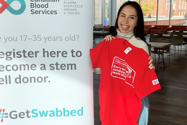Person holding a t-shirt in front of a Get Swabber Sign