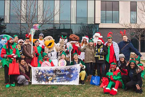 group photo of people dressed up as elves holding a banner that says Happy Holidays with the humber logo