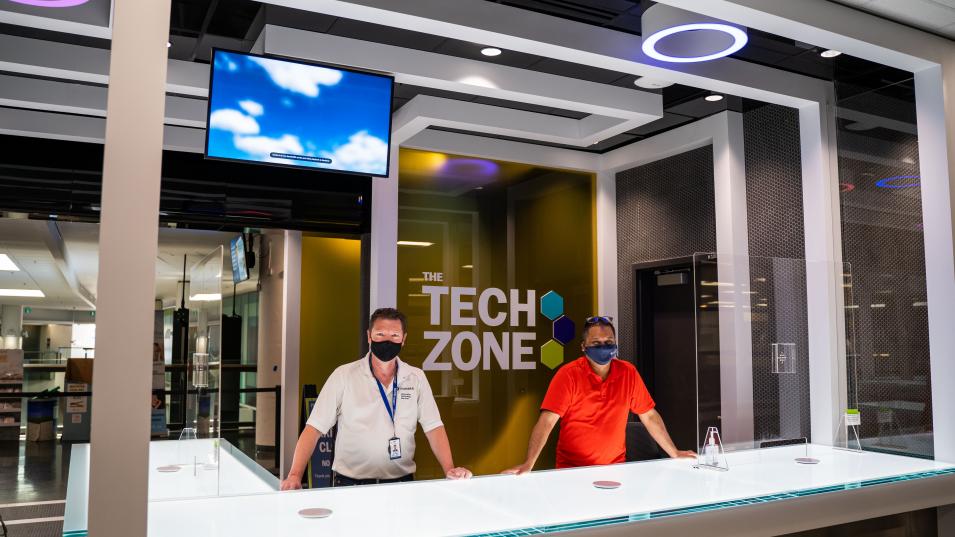 Two masked Humber IT staff members stand behind a big white desk at the futuristic Tech Zone