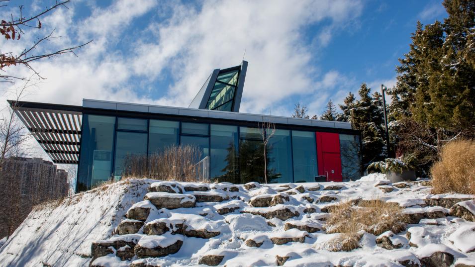 The Humber Arboretum building on a sunny day, surrounded by snow and footprints