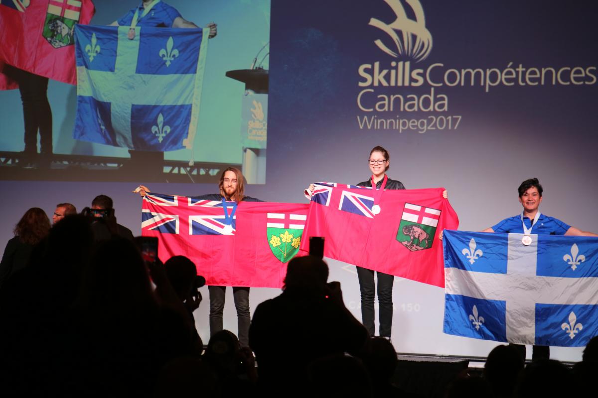 Three students holding provincial flags (Ontario, Manitoba, Quebec)