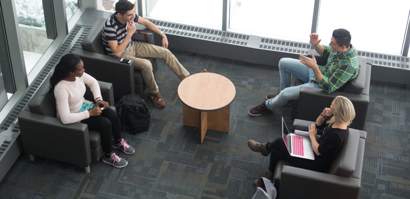 Aerial view of four students sitting in a lounge - snow is visable outside