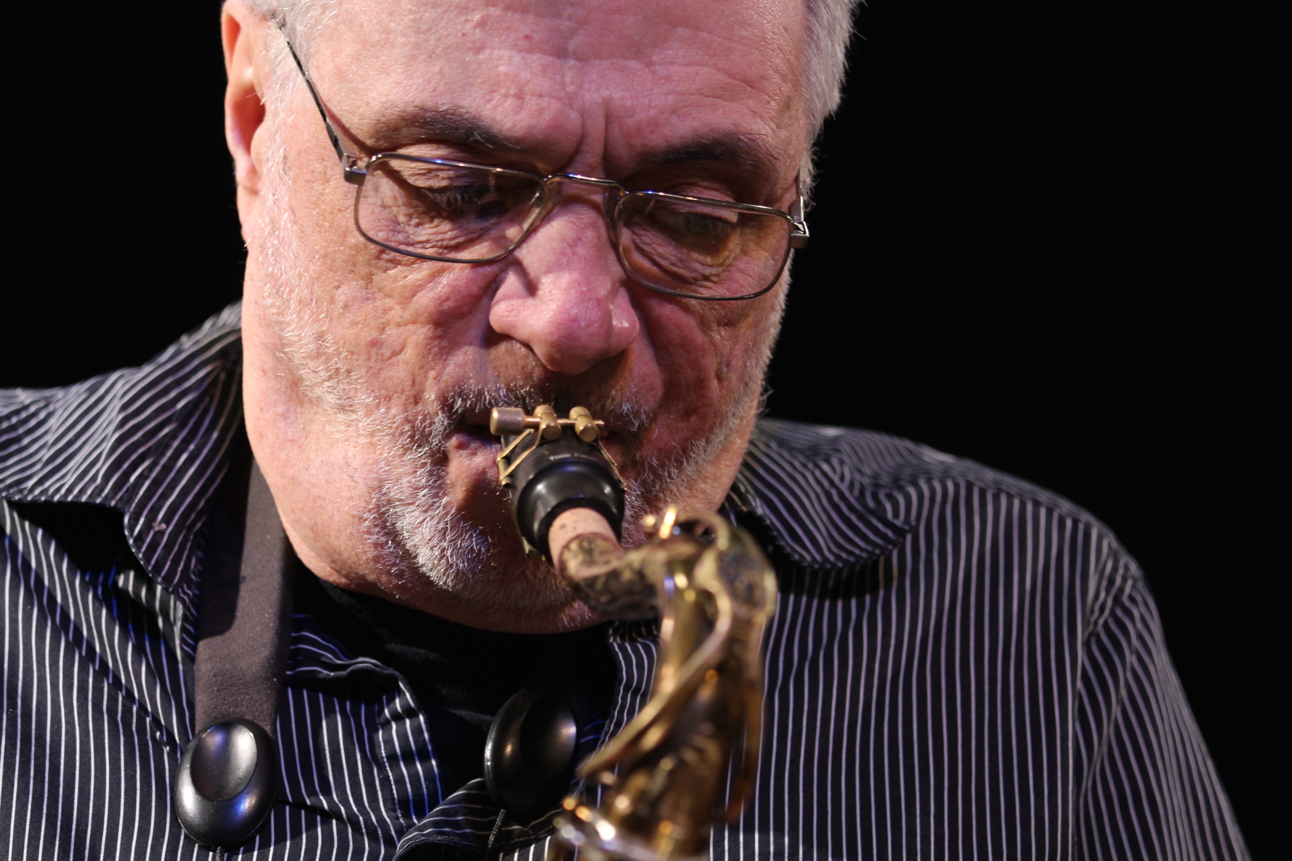 Closeup of man with grey hair and glasses playing a saxophone