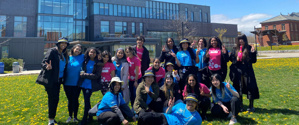 Students and Staff in blue and pink Orientation T-shirts taking a photo at the Lakeshore Courtyard outdoors in nice weather