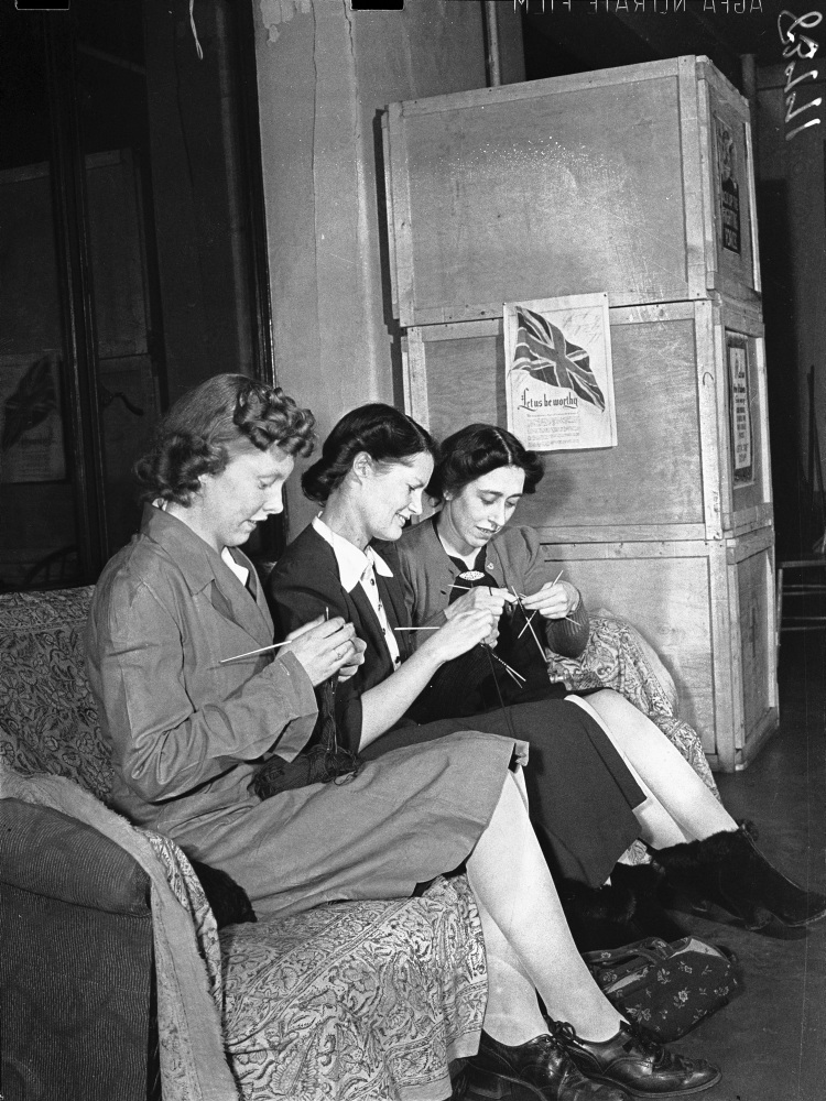 Black and white photo of three women knitting on bench