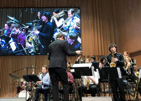 Man conducting a large band while a man playing the saxophone stands for a solo