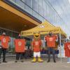Five people stand outside a large building holding orange shirts.