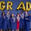 Several people wearing graduation gowns stand beneath a series of ballons spelling out the word Grad.