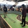 Two people stand on a miniature track while a car navigates the course.