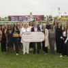 A group of people stand on a racetrack while three people holding a large cheque made out to Humber Polytechnic.