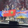 Three teams of two stand on a stage while holding their province’s flag. All of the people are wearing medals.