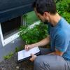 A person holding a clipboard is looking at a window on a home.