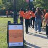 People wearing orange shirts walk past a sign with Walk for Reconciliation on it along with other information.