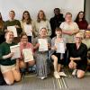 A large group of smiling people pose for a photo while holding certificates.