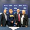Four people smile and pose for a photo while standing in front of a blue banner with the Humber College logo on it. 
