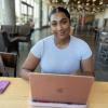 A smiling person sits in front of a laptop computer.