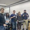 Several people stand together in a lab holding up pieces of technology.