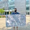 Newton Lew holds up a giant cheque for $5,000 from Humber College which hides most of his body.He's wearing a t-shirt and shorts