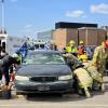 Students wearing firefighter gear work to remove a simulated patient from a vehicle.